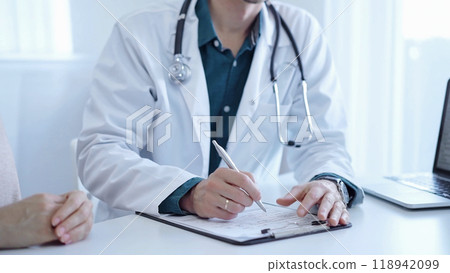 Doctor and a patient. The physician, wearing a white medical coat over a green shirt, is gesturing with his hands during a consultation in the clinic. Medicine 118942099
