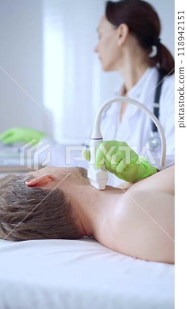 Doctor woman with green protective gloves performing an ultrasound scan of male patient breast lying down in clinic procedure cabinet. Cardiology diagnosis 118942151