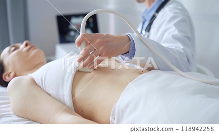 Doctor man, wearing white medical gloves, is using ultrasound equipment on the breast of a female patient lying down for a medical cardiology examination. Medicine concept 118942258