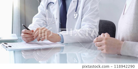 Doctor consulting patient. Male physician is gesturing with his hands over a glass desk while talking with a woman in a clinic, close up. Medicine concept Doctor consulting patient. Male physician is gesturing with his hands over a glass desk while talking with a woman in a clinic, close up. Medicine concept 118942290