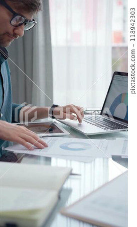 Businessman wearing green shirt and glasses is working with laptop computer and data analysis charts. Vertical business portrait Businessman wearing green shirt and glasses is working with laptop computer and data analysis charts. Vertical business portrait 118942303