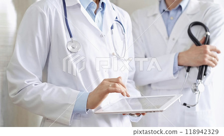 Two doctors wearing white coats and stethoscopes, using a digital tablet, discussing a patient's medical history. Medicine and science 118942329