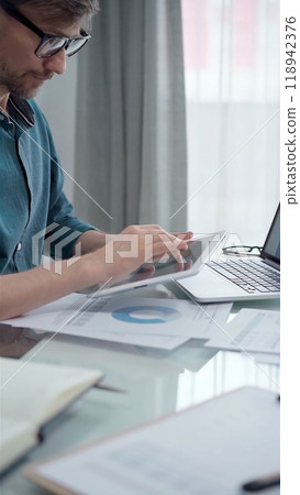 Businessman wearing green shirt and glasses is working with tablet computer and data analysis charts. Vertical business portrait 118942376