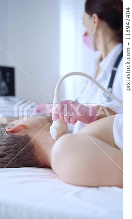 Doctor woman with pink medical gloves and mask performing neck ultrasound exam on male patient. Thyroid gland examination. Medicine concept 118942404