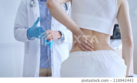 Doctor man wearing blue gloves examining back of female patient in clinic. Medicine and orthopedics Doctor man wearing blue gloves examining back of female patient in clinic. Medicine and orthopedics 118942441