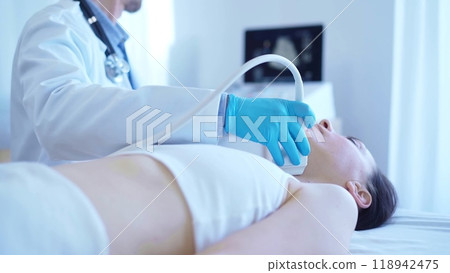 Doctor man with blue medical gloves is using ultrasound machine to examine neck of female patient lying down in clinic procedure cabinet. Medicine service 118942475