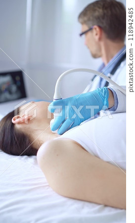 Doctor man wearing blue protective gloves is using ultrasound equipment on the neck of a patient woman, lying for examination. Medicine concept Doctor man wearing blue protective gloves is using ultrasound equipment on the neck of a patient woman, lying for examination. Medicine concept 118942485