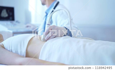 Doctor man wearing a white coat using an ultrasound machine on a female patient examining internal organs. Preventive therapy in medicine Doctor man wearing a white coat using an ultrasound machine on a female patient examining internal organs. Preventive therapy in medicine 118942495