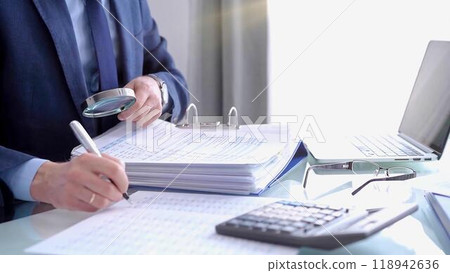 Businessman using a calculator and magnifying glass while analyzing financial documents at desk in fair modern office. Audit and taxes in business 118942636
