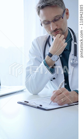 Doctor and a patient. The physician, wearing a white medical coat over a green shirt, gesturing with his hands during a consultation in the clinic. Medicine concept 118942885