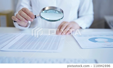 Businesswoman with white blues is analyzing financial data on a spreadsheet using a magnifying glass. Audit and taxes 118942896