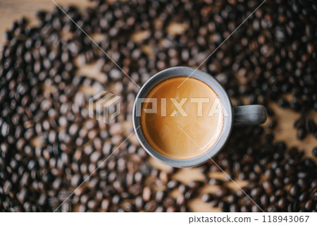 A cup of coffee surrounded by aromatic coffee beans on a wooden surface 118943067
