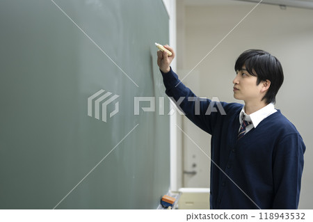 A male high school student writing the national language exam on the blackboard in the classroom with chalk A male high school student writing the national language exam on the blackboard in the classroom with chalk 118943532