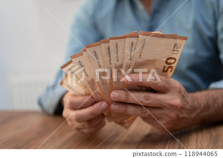 Person fanning out 50 euro banknotes on a wooden table. Depicts financial transactions, currency management, and economic stability Person fanning out 50 euro banknotes on a wooden table. Depicts financial transactions, currency management, and economic stability 118944065