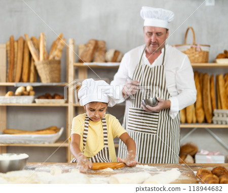 Little daughter and father make dough together in bakery kitchen Little daughter and father make dough together in bakery kitchen 118944682