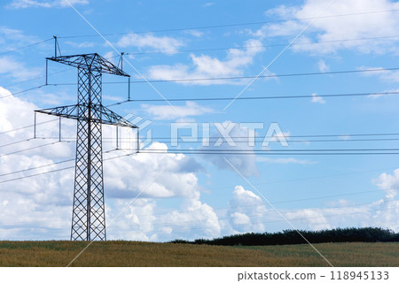 Electricity concept. High voltage power line pylons, electrical tower on a green field with blue sky. 118945133