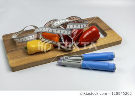 Ozempic Insulin injection pen for diabetics and weight loss and a cutting board with vegetables and a measuring tape. Ozempic Insulin injection pen for diabetics and weight loss and a cutting board with vegetables and a measuring tape. 118945263