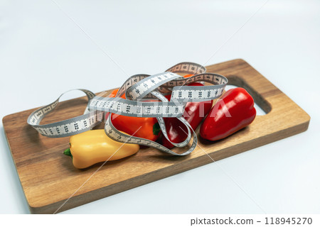 Cutting board with vegetables and a measuring tape. Concept of diet and weight loss Cutting board with vegetables and a measuring tape. Concept of diet and weight loss 118945270