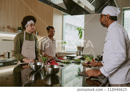 Chef explaining recipe details to his cooks who listening him and ready to cook dish 118946625