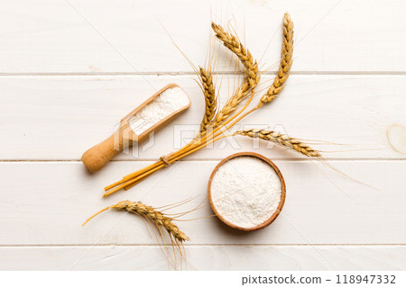 Flat lay of Wheat flour in wooden bowl with wheat spikelets on colored background. world wheat crisis Flat lay of Wheat flour in wooden bowl with wheat spikelets on colored background. world wheat crisis 118947332