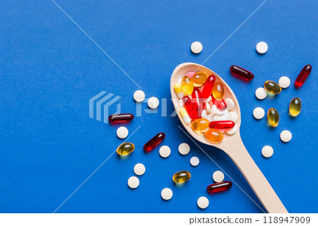 Vitamin capsules in a spoon on a colored background. Pills served as a healthy meal. Red soft gel vitamin supplement capsules on spoon Vitamin capsules in a spoon on a colored background. Pills served as a healthy meal. Red soft gel vitamin supplement capsules on spoon 118947909