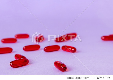 Heap of red pills on colored background. Tablets scattered on a table. Pile of red soft gelatin capsule. Vitamins and dietary supplements concept 118948026