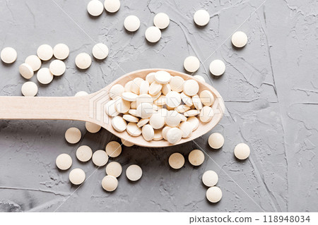 Heap of white pills on colored background. Tablets scattered on a table. Pile of red soft gelatin capsule. Vitamins and dietary supplements concept 118948034