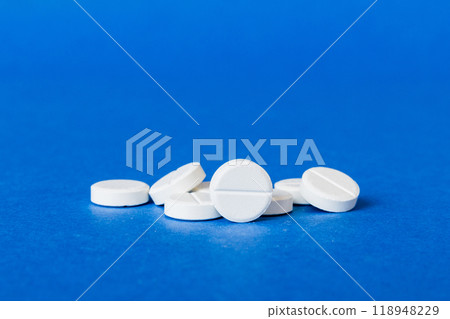 Heap of white pills on colored background. Tablets scattered on a table. Pile of red soft gelatin capsule. Vitamins and dietary supplements concept Heap of white pills on colored background. Tablets scattered on a table. Pile of red soft gelatin capsule. Vitamins and dietary supplements concept 118948229