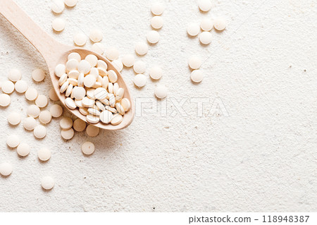 Heap of white pills on colored background. Tablets scattered on a table. Pile of red soft gelatin capsule. Vitamins and dietary supplements concept Heap of white pills on colored background. Tablets scattered on a table. Pile of red soft gelatin capsule. Vitamins and dietary supplements concept 118948387