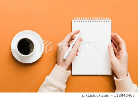 Woman hand with pencil writing on notebook and hold coffee cup. Woman working on office table with coffee 118948462