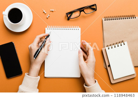 Woman hand with pencil writing on notebook and hold coffee cup. Woman working on office table with coffee Woman hand with pencil writing on notebook and hold coffee cup. Woman working on office table with coffee 118948463