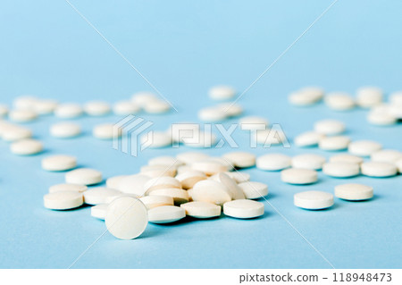 Heap of white pills on colored background. Tablets scattered on a table. Pile of red soft gelatin capsule. Vitamins and dietary supplements concept Heap of white pills on colored background. Tablets scattered on a table. Pile of red soft gelatin capsule. Vitamins and dietary supplements concept 118948473