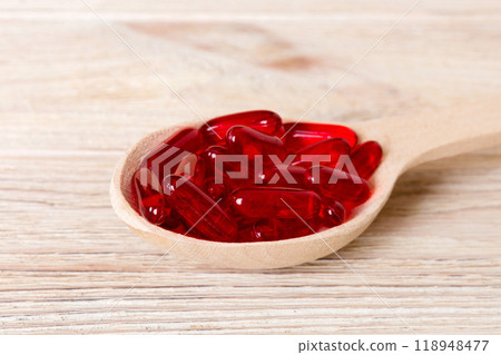 Vitamin capsules in a spoon on a colored background. Pills served as a healthy meal. Red soft gel vitamin supplement capsules on spoon 118948477