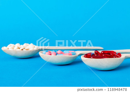 Vitamin capsules in a spoon on a colored background. Pills served as a healthy meal. Red soft gel vitamin supplement capsules on spoon 118948478