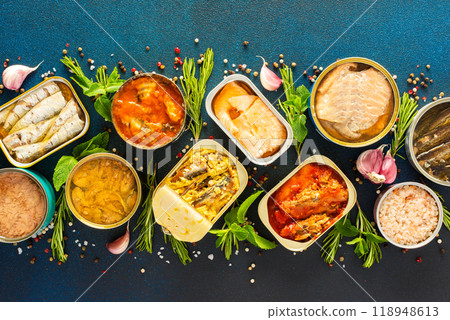 Different open tin cans with canned fish like salmon, mackerel, sprat, sardine, tuna, and herring, among spices and herbs on a blue background, Different open tin cans with canned fish like salmon, mackerel, sprat, sardine, tuna, and herring, among spices and herbs on a blue background, 118948613