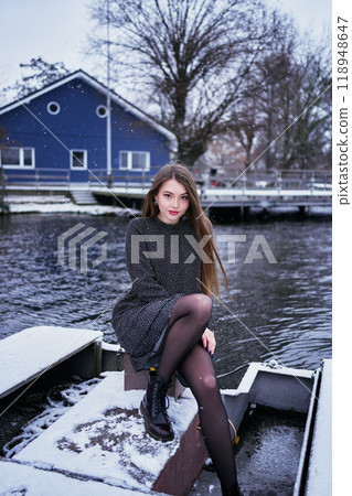 beautiful young woman with long blond hair in a light dress under the snowfall on the pier of the winter lake beautiful young woman with long blond hair in a light dress under the snowfall on the pier of the winter lake 118948647