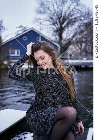 beautiful young woman with long blond hair in a light dress under the snowfall on the pier of the winter lake beautiful young woman with long blond hair in a light dress under the snowfall on the pier of the winter lake 118948649