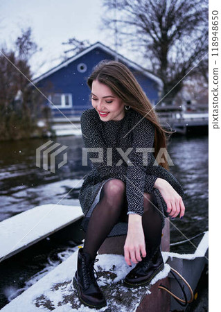 beautiful young woman with long blond hair in a light dress under the snowfall on the pier of the winter lake 118948650