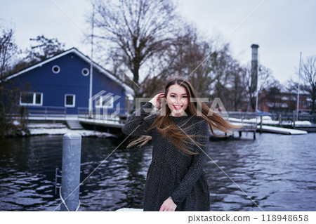 beautiful young woman with long blond hair in a light dress under the snowfall on the pier of the winter lake 118948658