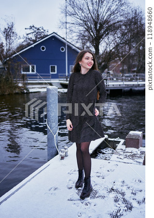 beautiful young woman with long blond hair in a light dress under the snowfall on the pier of the winter lake beautiful young woman with long blond hair in a light dress under the snowfall on the pier of the winter lake 118948660