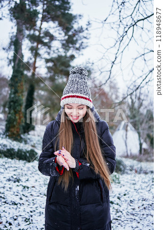 a beautiful young girl with long blond hair in a hat and a long down jacket plays with snow and enjoys winter nature 118948677