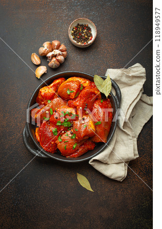 Raw uncooked chopped pieces of meat marinated with seasonings and parsley in black casserole dish top view on dark rustic background. Cooking ragout stew with marinated meat fillet pieces 118949577