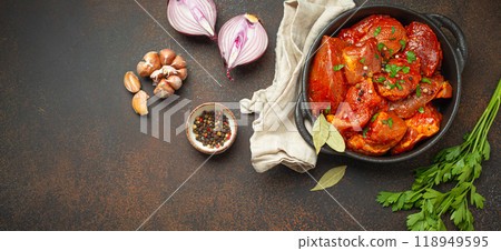 Cooking hearty meat stew. Raw uncooked chopped pieces of meat marinated with seasonings and parsley in black casserole dish top view, ingredients on dark rustic background. Space for text Cooking hearty meat stew. Raw uncooked chopped pieces of meat marinated with seasonings and parsley in black casserole dish top view, ingredients on dark rustic background. Space for text 118949595