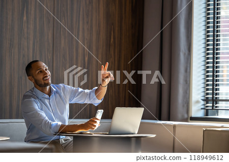 Dark skinned businessman in formal shirt using laptop and mobile phone in office cafe 118949612