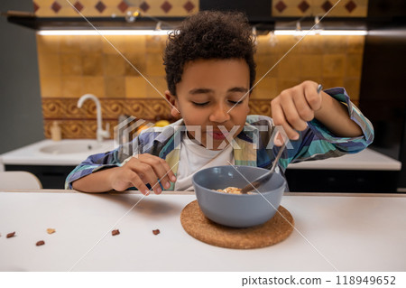 Dark-skinned boy sitting at the table and eating breakfast Dark-skinned boy sitting at the table and eating breakfast 118949652
