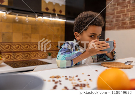 Curly-haired boy sitting in the kitchen and drinking milk Curly-haired boy sitting in the kitchen and drinking milk 118949653