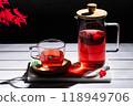 Red fruit infusion in crystal glass and pitcher on white wooden table on dark background. 118949706