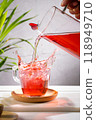 Pouring red fruit infusion and splashing from pitcher into glass on light background. Vertical format. 118949710