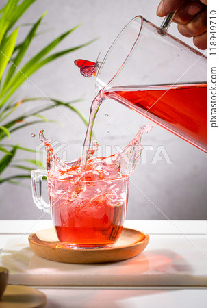 Pouring red fruit infusion and splashing from pitcher into glass on light background. Vertical format. 118949710