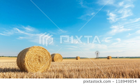 Hay Bales in a Golden Field Under a Blue Sky with White Clouds and a Windmill in the Distance 118949854